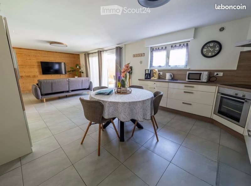 Open-plan living and dining area with a sofa, dining table, chairs, television, and kitchen appliances including an oven and microwave.