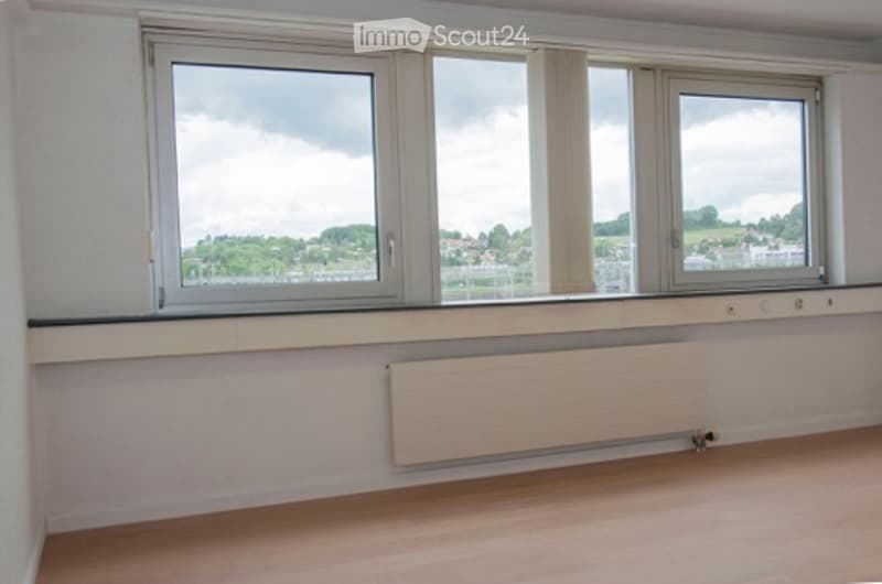 white walls, three large windows, radiator, wooden floor