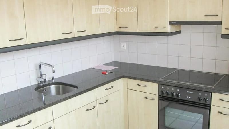 Modern kitchen with light wood cabinets, granite countertops, stainless steel sink, and built-in oven.