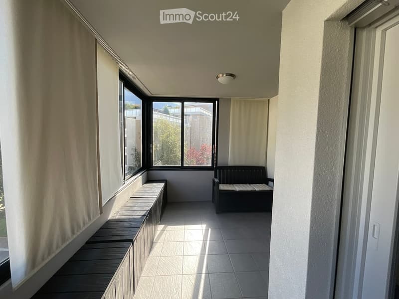 Balcony with tiled floor, large windows, a black sofa, and a bench along the wall.