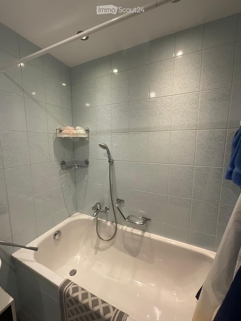 Modern bathroom with a white bathtub, tiled walls, a showerhead, and a towel on the side.
