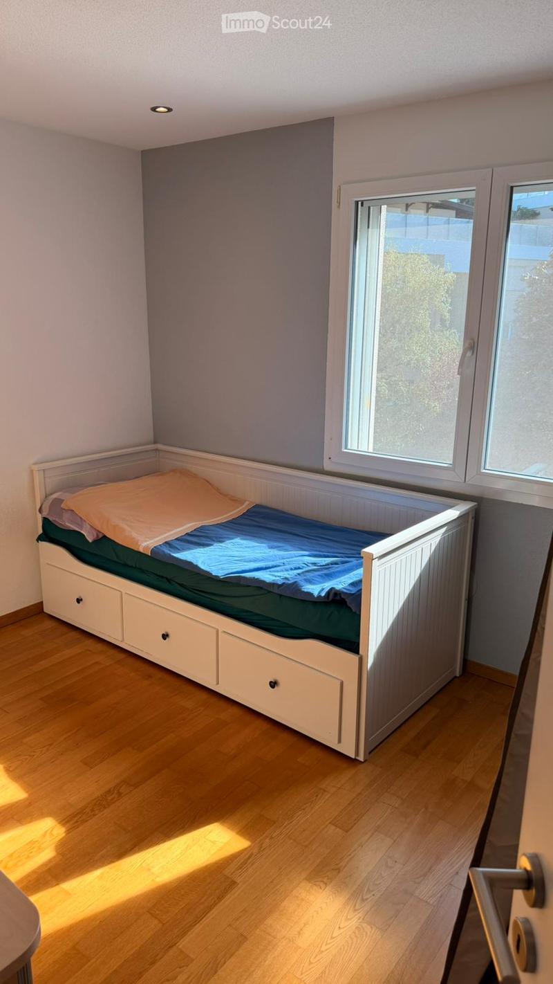 Cozy bedroom with a single bed featuring a white frame and drawers, blue and green bedding, and natural light from two windows.