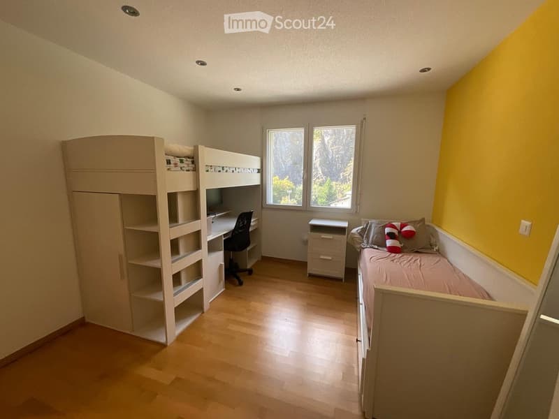 Cozy bedroom with wooden flooring, bunk bed, desk, chair, wardrobe, and nightstand. Features a single bed with pillows and a small nightstand.