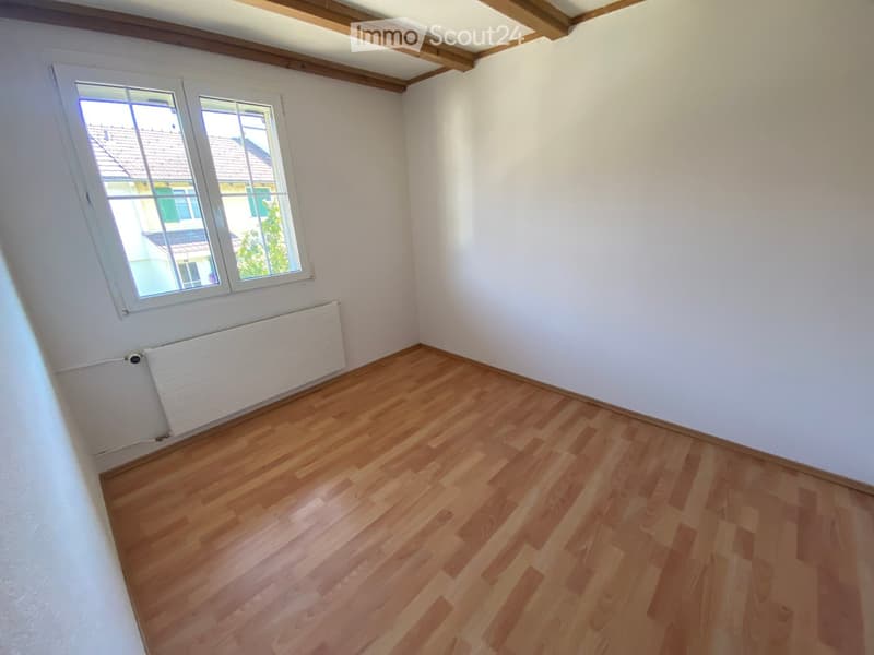 Empty room with wooden flooring, white walls, and a window with white frame. A radiator is visible below the window.