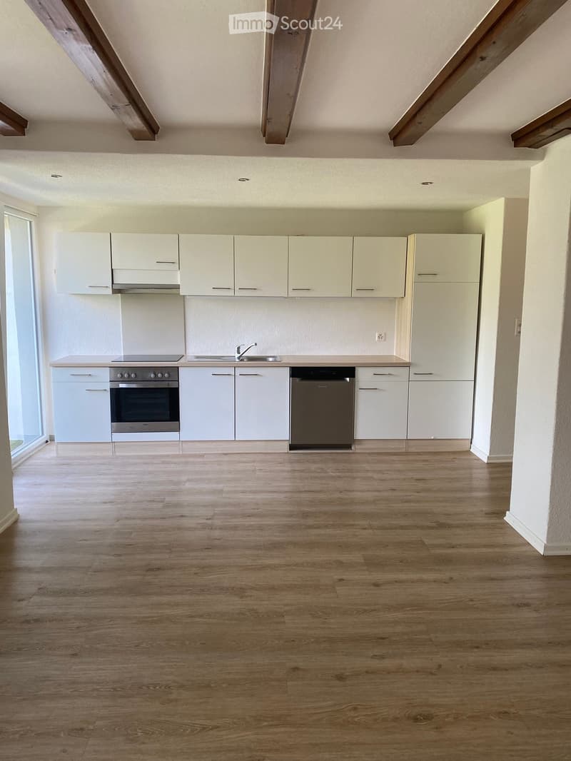 Empty kitchen with white cabinets, stainless steel appliances, and wooden flooring.