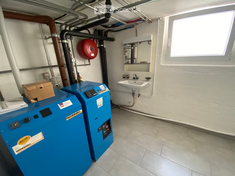 Bathroom with a sink, faucet, mirror, water heater, and a fire extinguisher mounted on the wall. The room has exposed pipes and a window at the top right.