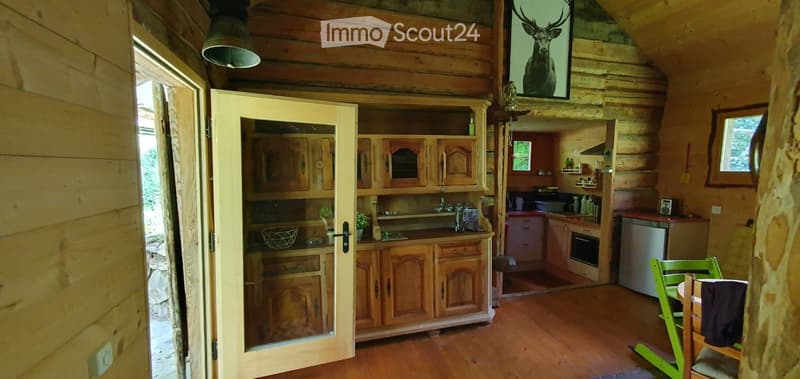 Cozy log cabin interior with wooden walls, a kitchen area featuring cabinets, sink, and appliances, and a dining area with a table and chairs.