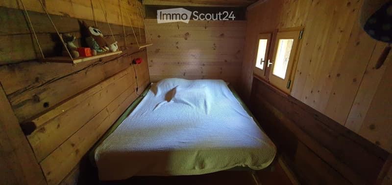 Cozy wooden bedroom with a single bed, a small shelf holding toys, and a window with wooden shutters.