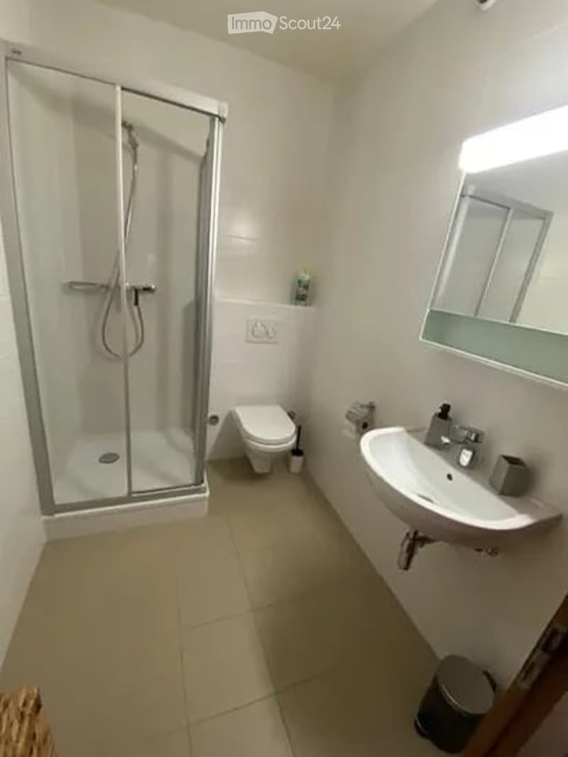 Modern bathroom with a glass-enclosed shower, toilet, sink, and mirror. The space is clean and well-lit with tiled floors and walls.