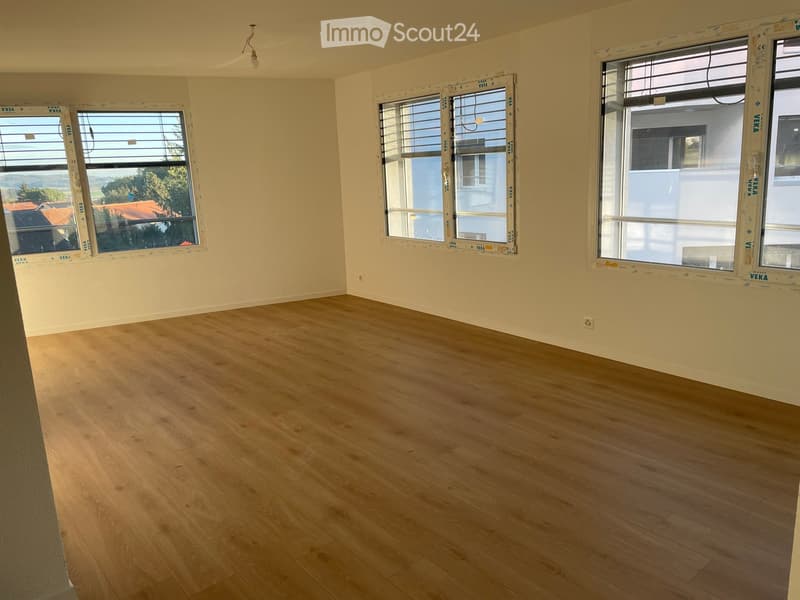 Empty room with light wooden flooring and three large windows with blinds, walls painted in a light color.