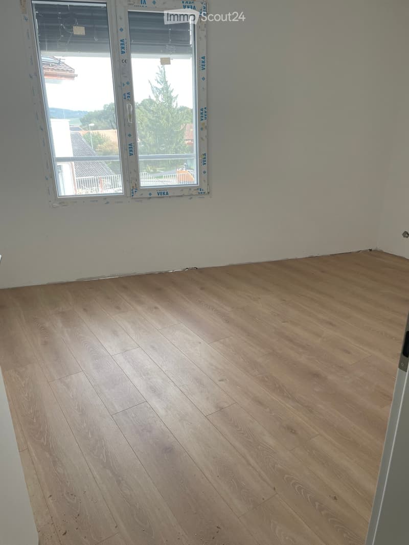 Empty room with light wooden flooring and white walls, featuring a large window with protective film.