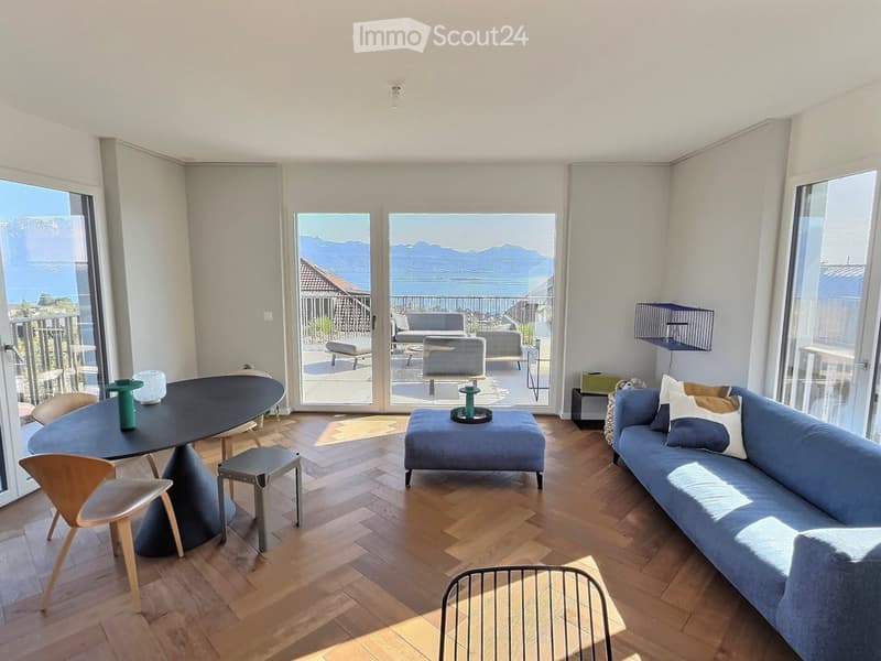 Modern living room with wooden flooring, large windows offering a scenic view, a blue sofa, a coffee table, and a dining table with chairs.
