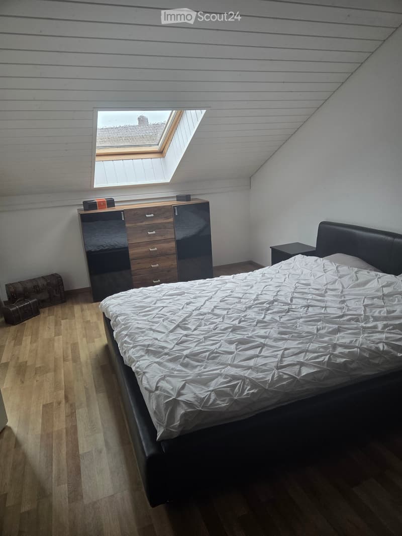 Bedroom with a large bed, nightstand, wardrobe, chest of drawers, and two suitcases on the floor.