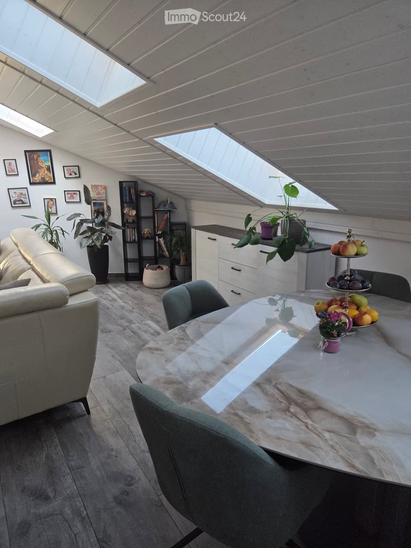 Bright, modern living room with a skylight ceiling, a cream-colored sofa, a marble dining table with four chairs, a cabinet, and several potted plants.