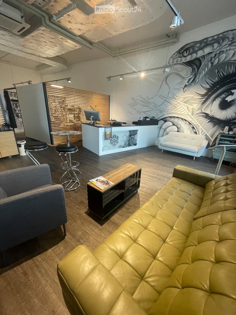 Modern interior with a large eye mural on the wall, a reception desk, a yellow leather sofa, a small table with a magazine, and two stools near the desk.