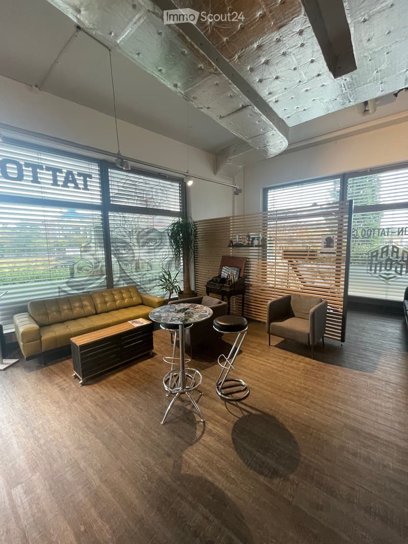 Modern living room with wooden flooring, large windows, a yellow sofa, a small round table, two high stools, and a small plant in the corner.