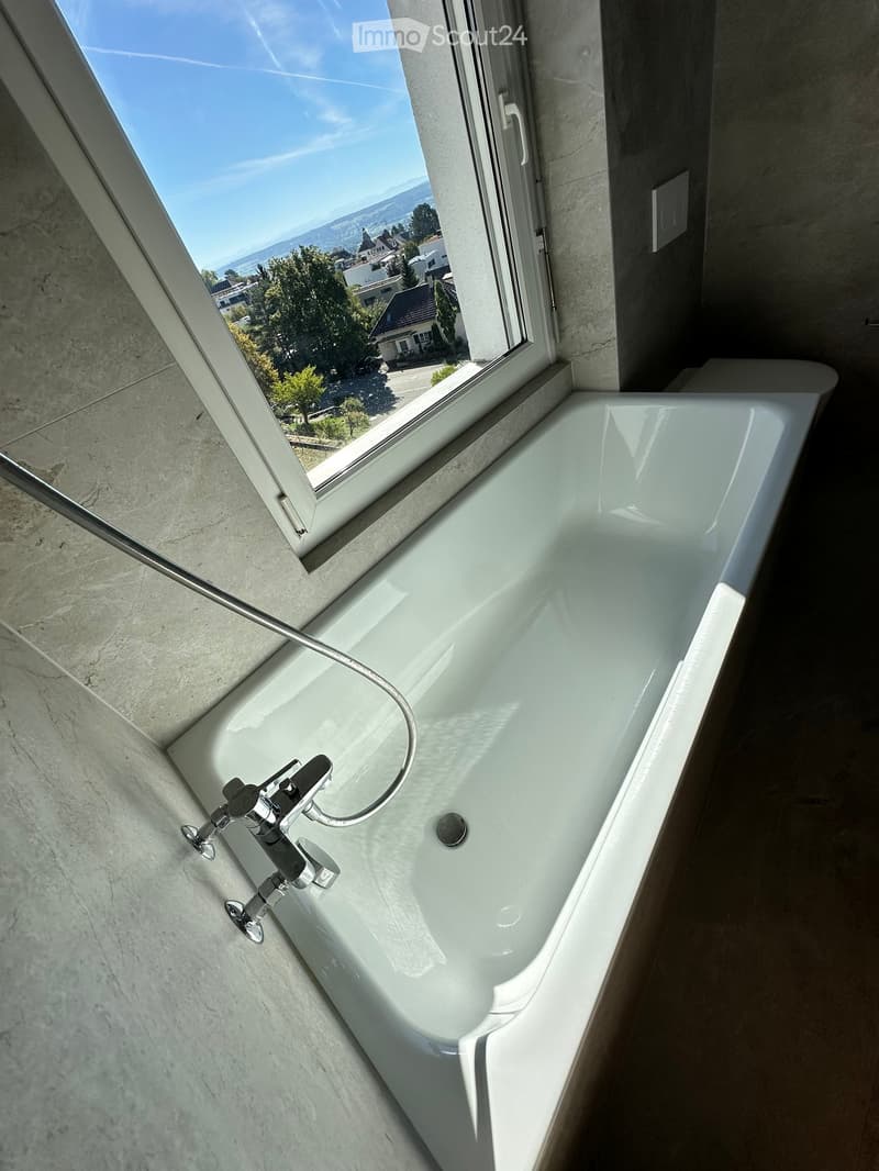 Modern bathtub with sleek faucet, large window offering scenic view of the landscape.