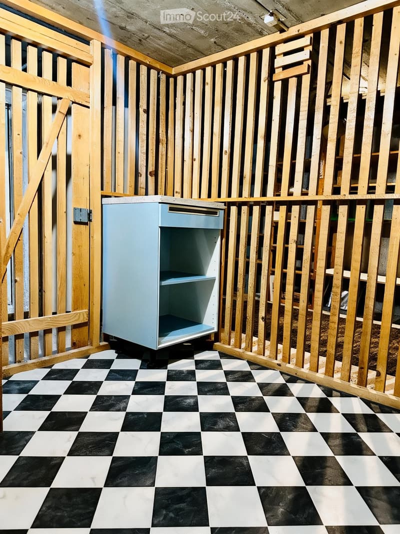 Empty room with exposed wooden framing, black and white checkered floor, and a single light blue cabinet with shelves.