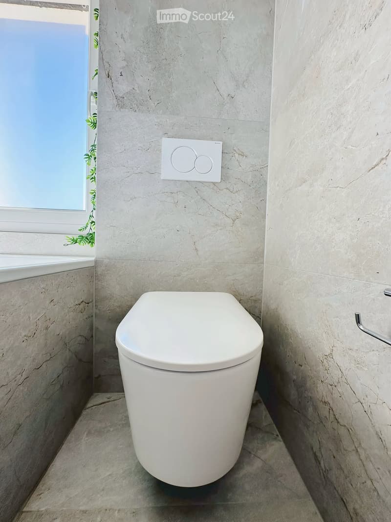 Modern bathroom with marble walls and floor, featuring a white toilet and a light switch on the wall.