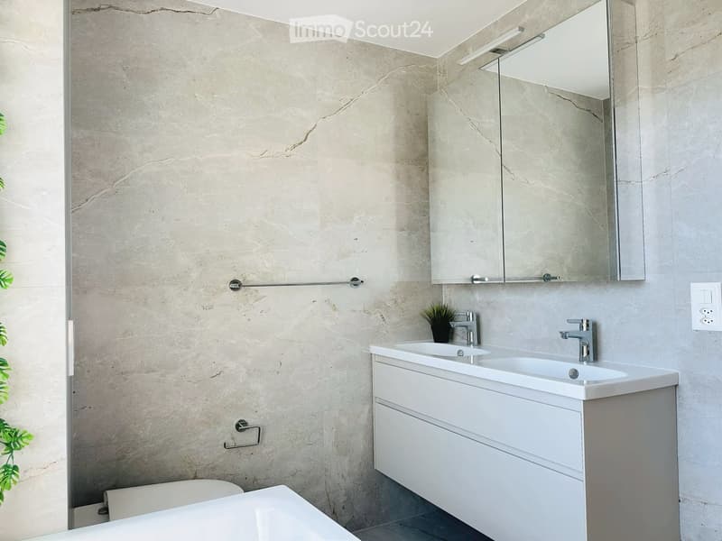 Modern bathroom with marble walls, a white bathtub, a double sink vanity with mirrored cabinet, and sleek chrome faucets.