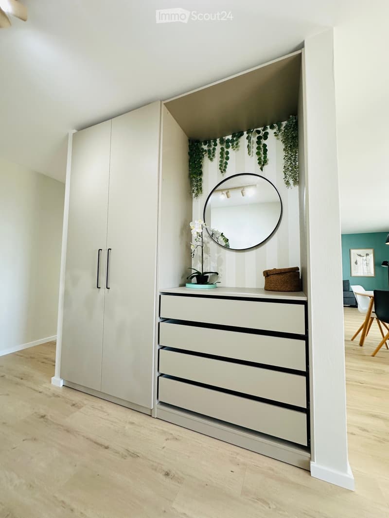 Modern hallway with a built-in wardrobe and a vanity area featuring a round mirror, drawers, and decorative plants.