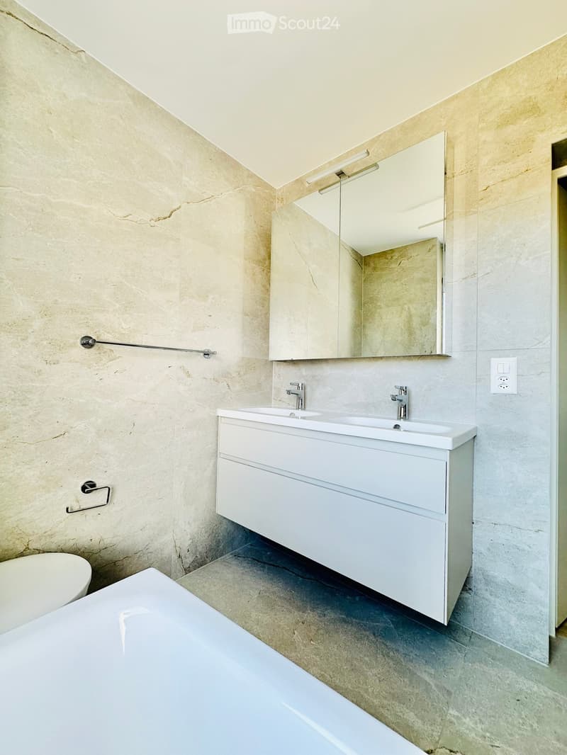 Modern bathroom with marble walls, a white sink cabinet, a large mirror, a bathtub, and a toilet.