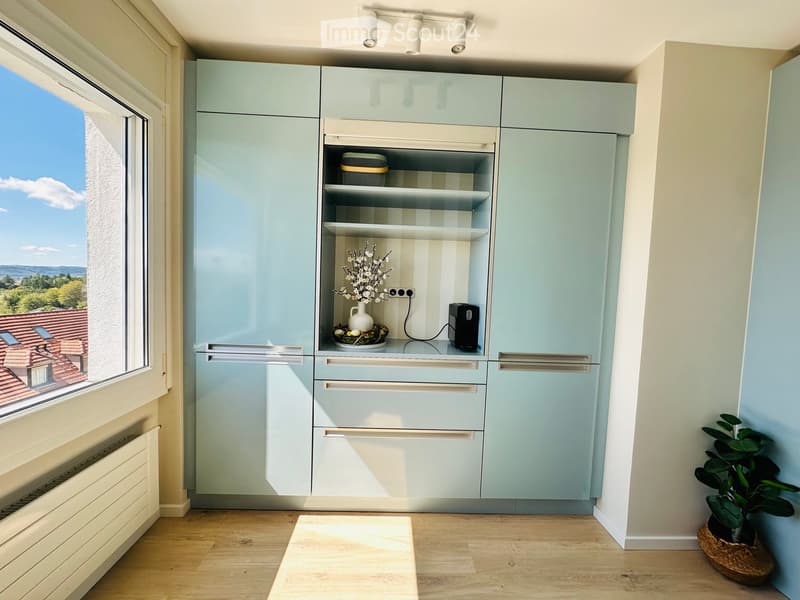 Modern kitchen with light blue cabinets, a window offering a scenic view, and a small decorative setup on the counter.