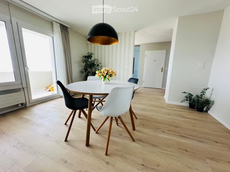 Dining room with a round white table, four chairs, a flower vase with tulips, a pendant light, and wooden flooring.