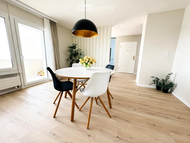 Modern dining room with light wooden flooring, white dining table, four chairs, pendant light, and decorative plants.