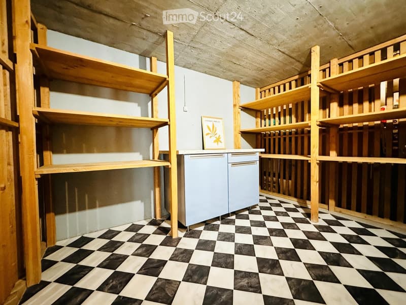 A small, modern room with black and white checkered flooring, wooden shelves, a light blue fridge, and a framed picture on the counter.