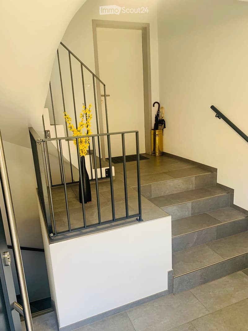 Staircase with modern metal railing, beige tiled steps, and a vase with yellow flowers on the landing.