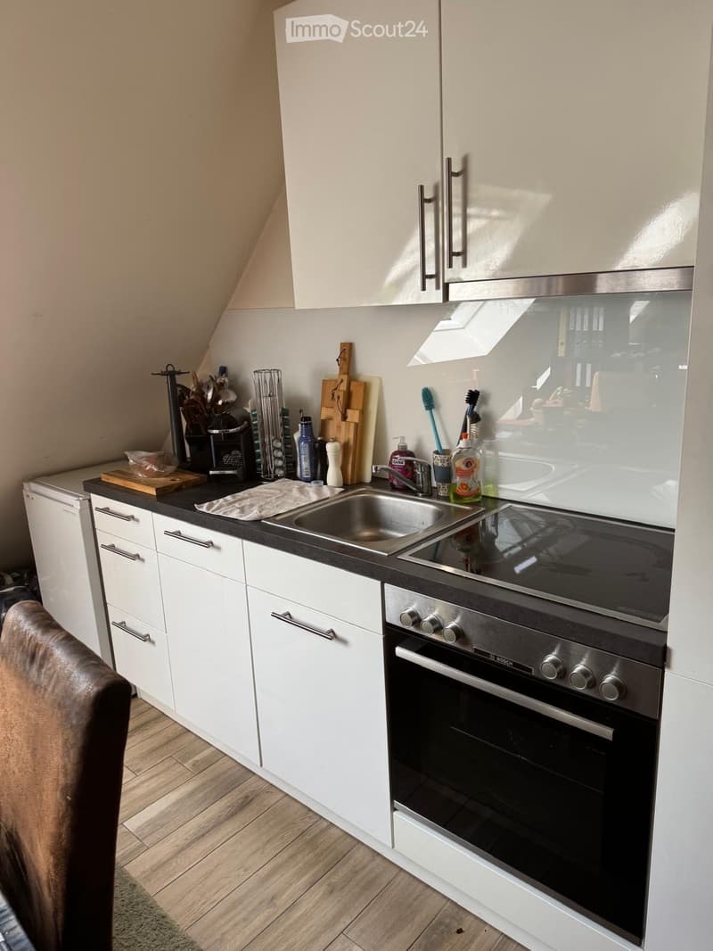Modern kitchen with white cabinets, stainless steel sink, oven, and various utensils on the counter.