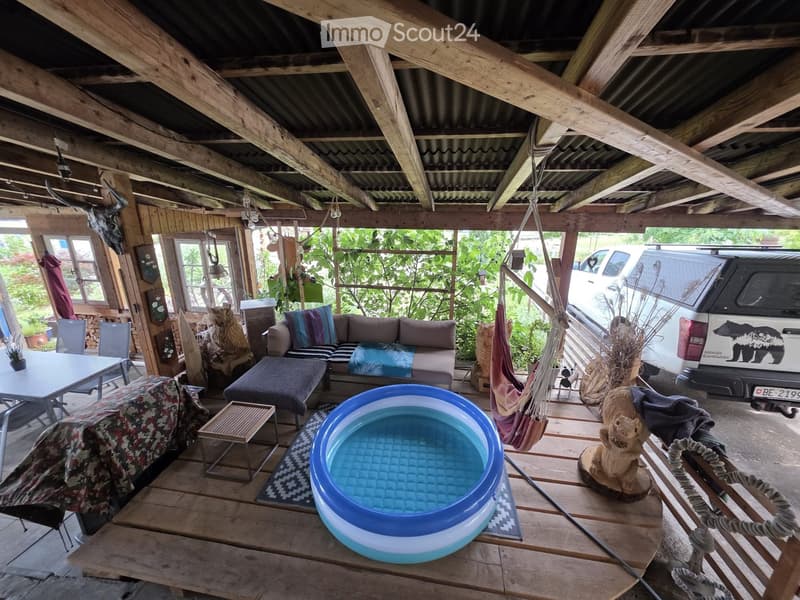 Wooden outdoor area with exposed beams, featuring a sofa, ottoman, small table, chairs, hammock, small pool, and decorative items.