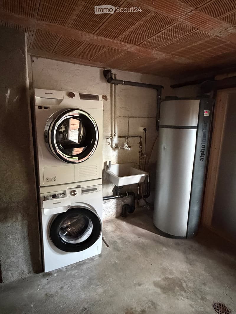 Utility room with a stacked washing machine and dryer, water heater, and sink.