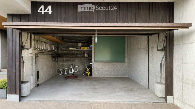 Open garage with concrete floor, wooden door frame, shelves, and tools.