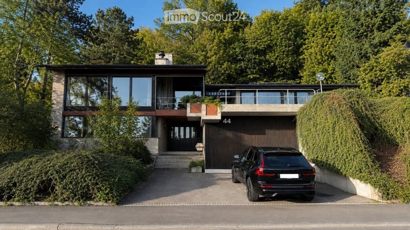 Modern two-story house with large windows, a garage, and a parked car in front.
