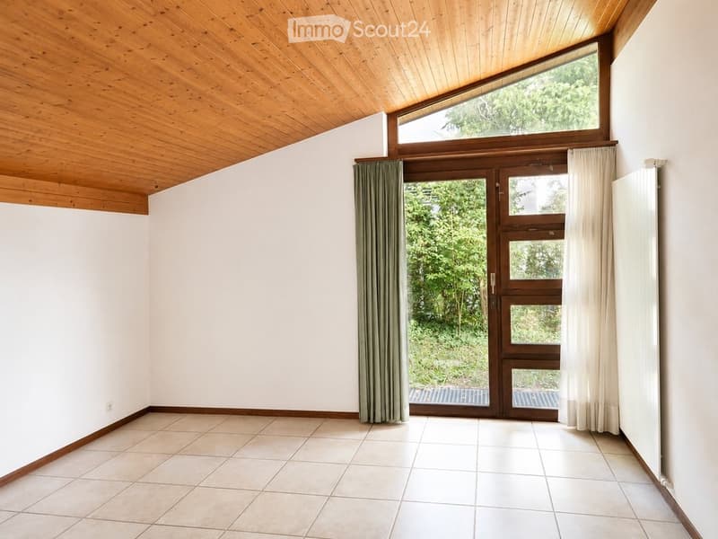 Empty room with white walls, wooden ceiling, tiled floor, large window, and double doors leading outside.