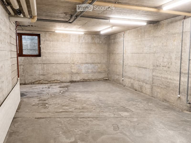 Empty basement with concrete walls and floor, exposed pipes, and a small window.