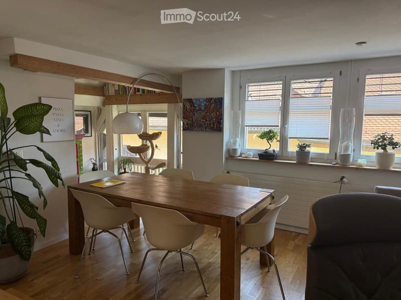 Bright dining area with wooden table, white chairs, cat tree, large floor lamp, and potted plants on windowsill.