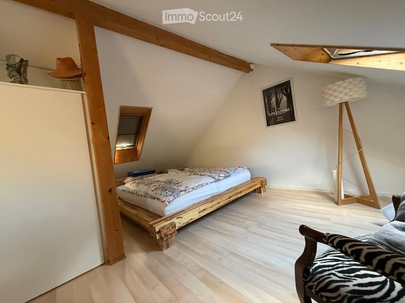 Cozy attic bedroom with wooden bed, chair, floor lamp, mirror, and artwork on the wall.
