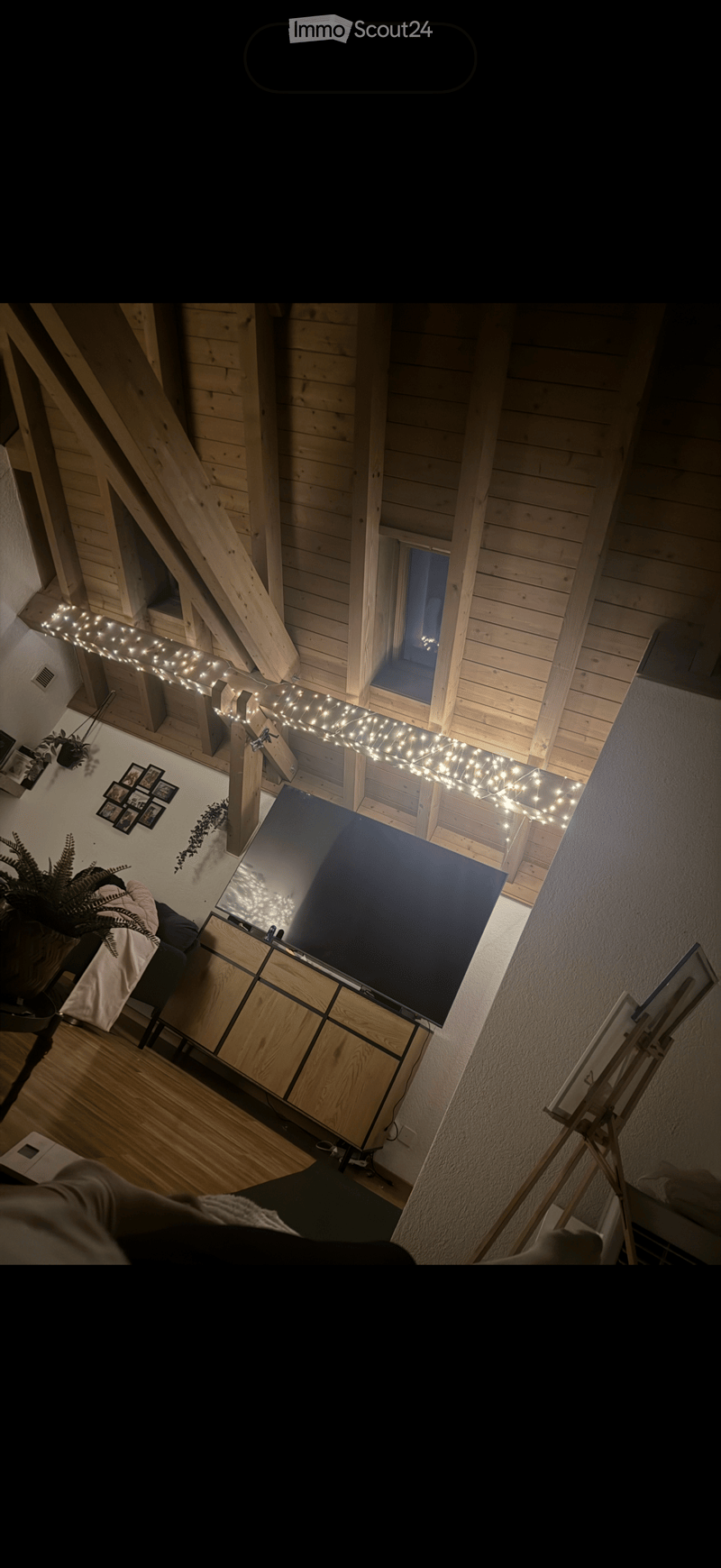 A modern living room with wooden beams, a large screen, a sofa, a table, and decorative lights.