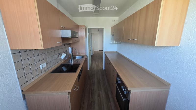 Modern kitchen with wooden cabinets, a sink, and an oven. The floor is wooden, and the walls are tiled in the kitchen area.