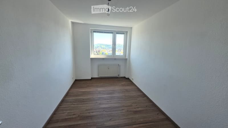 Empty room with wooden flooring, white walls, a window with a view, and a radiator.