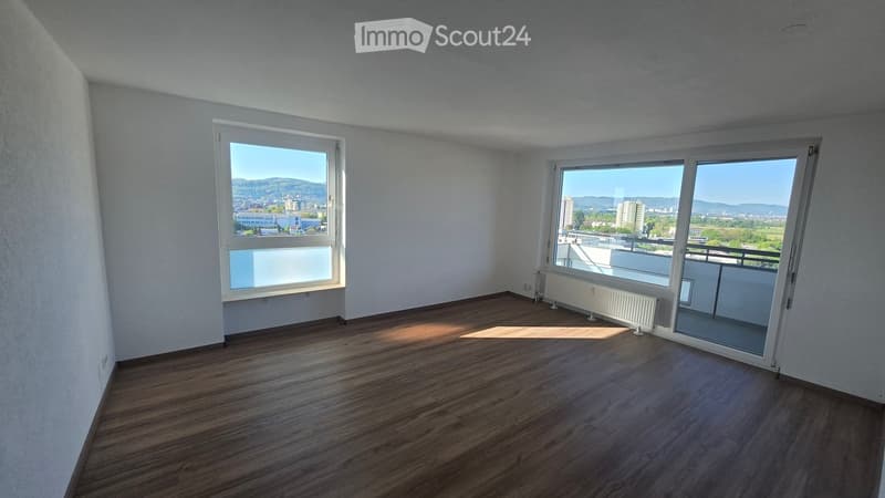 Empty room with wooden flooring, white walls, large windows, and a sliding glass door leading to a balcony.