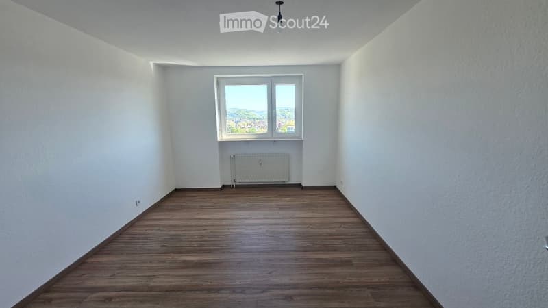 Empty room with wooden flooring, white walls, and a window offering a view of the landscape.