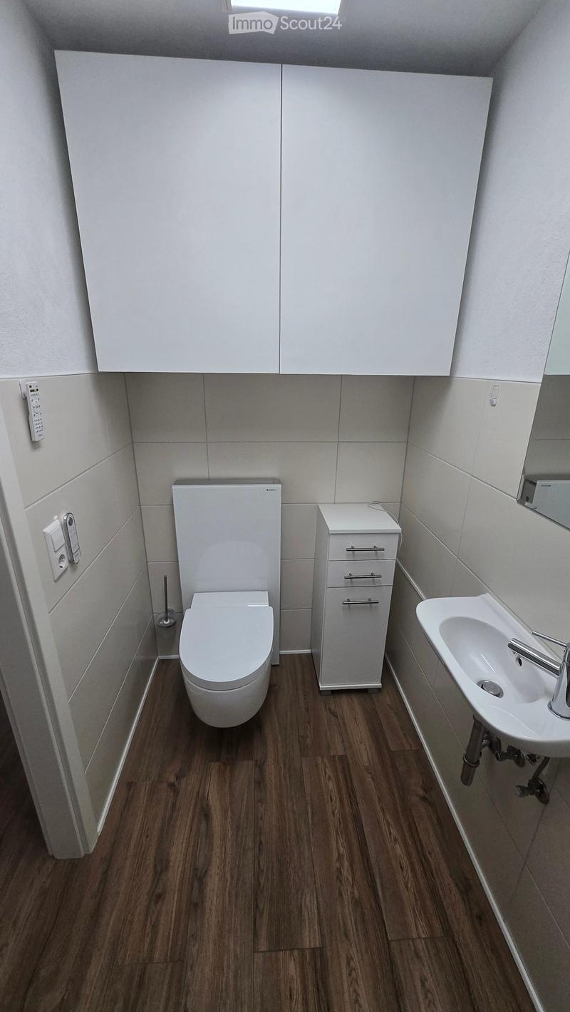 Modern bathroom with white tiled walls, wooden flooring, toilet, sink, and cabinet.