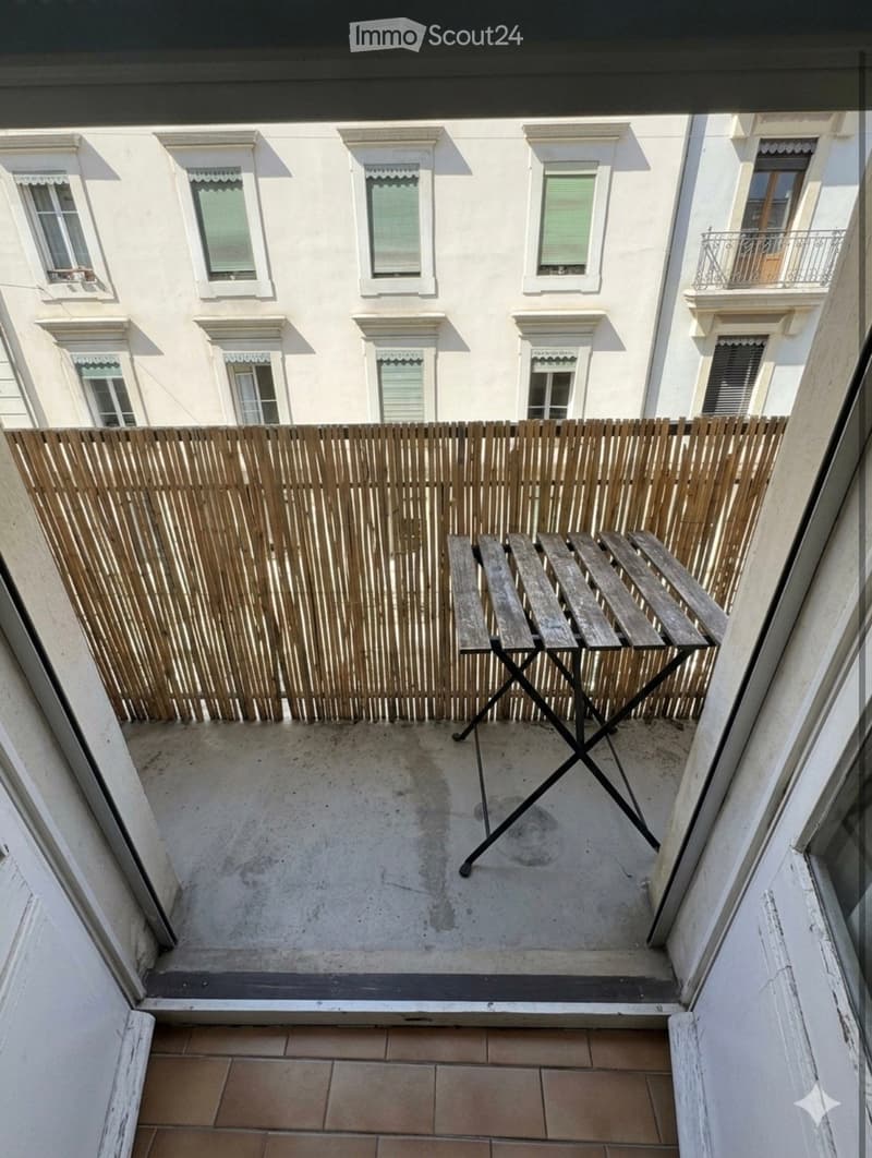 Balcony with wooden fence, concrete floor, and a single wooden table.