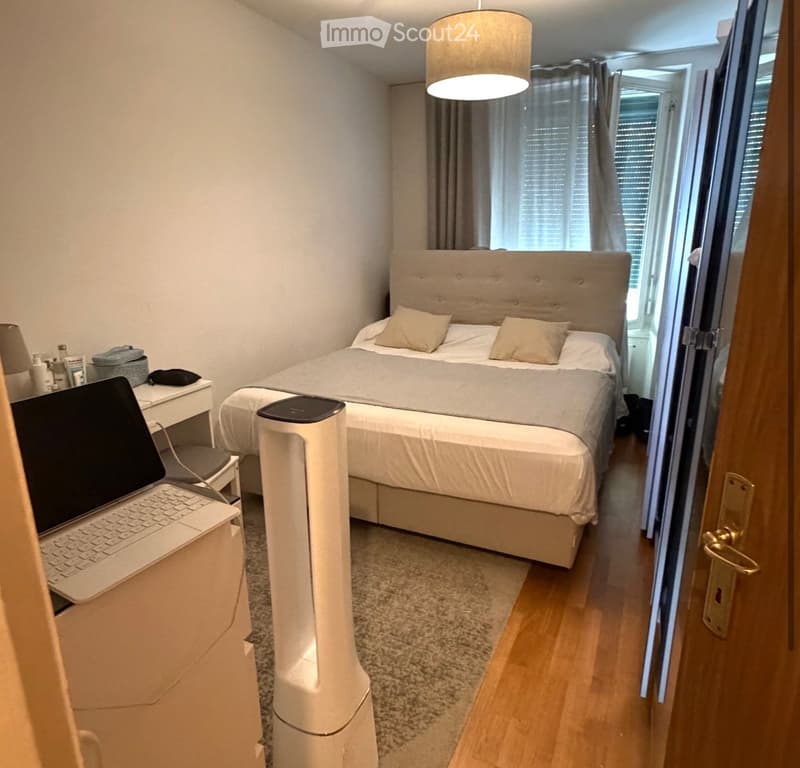 Modern bedroom with a large bed, nightstand, laptop, air purifier, and large windows with curtains.