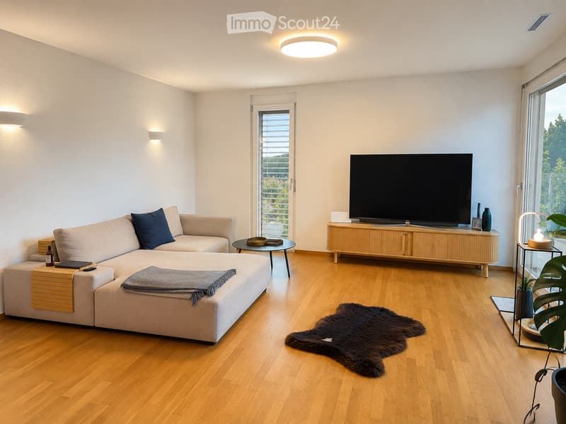 Modern living room with light wooden flooring, a large sectional sofa, a coffee table, a television on a wooden stand, and a fur rug.