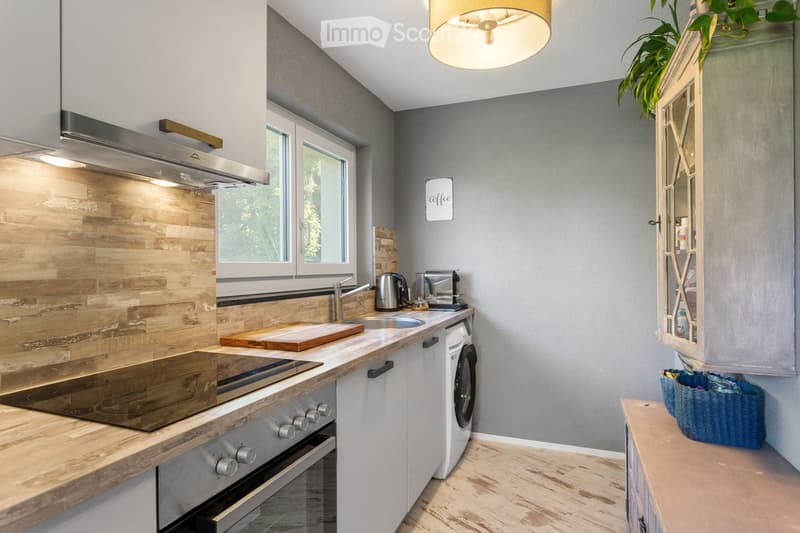 Modern kitchen with wooden countertops, stainless steel appliances, and a built-in oven. Features include a sink with a faucet, a wooden cutting board, a washing machine, and a glass-fronted cabinet.